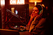 © Seventyfour - Modern young adult woman working on radio broadcast in amateur home studio at night turning on her favourite music playlist