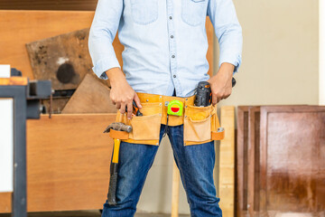 Handyman manual worker in tools belt and holding drill in his hands, Carpenter working with equipment in wood workshop, man doing woodwork in carpentry shop