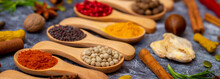 A Set Of Spices On A Gray Background. Variety Of Spices From India. Food Decoration Design. Various Spices, Peppers And Herbs Close-up Top View. Set Of Peppers, Salt, Herbs And Spices For Cooking.