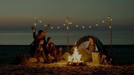 group of young people having camp on the beach at night