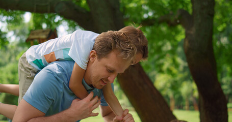 Wall Mural - Playful son riding on back blond man closeup. Smiling father lift up cute boy.