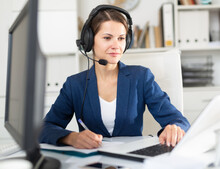 Smiling Young Female Operator Talking With Customer Using Headset At Company Office
