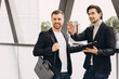 © anatoliycherkas - Two modern happy businessmen with documents folder discussing something against the background of urban offices and buildings