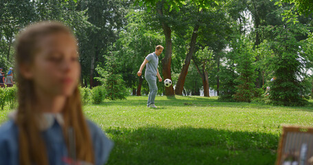 Wall Mural - Young father passing ball active son behind resting daughter in park.