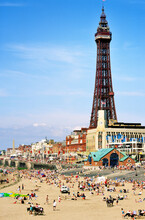 English Seaside Summer Holiday. People Sunbathing On Blackpool Beach Beneath Blackpool Tower, Lancashire, England.