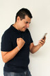 © Arlette - Latin dark-haired adult man with black hair receives and sends messages from his cell phone very excited and happy makes purchases online in app and works online