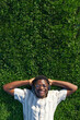 © Daniel - Top view of black man relaxing. Happy black male lying on grass listen to music with headphones. Copy space Vertical