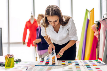 Wall Mural - Portrait of young beautiful pretty owner business woman fashion designer stylish sitting and working.Attractive young designer girl use desktop conputer and colorful fabrics at fashion studio