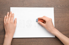 Woman Erasing Word On Sheet Of White Paper At Wooden Table, Top View