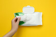 © New Africa - Woman taking wet wipe from pack on yellow background, top view