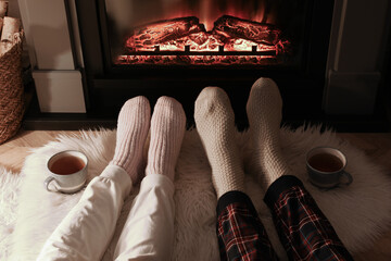 Poster - Couple in knitted socks near fireplace at home, closeup of legs