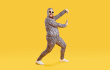 Funny Chubby Guy In Crazy Costume Having Fun In Modern Fashion Studio. Happy Cheerful Confident Fat Man Wearing Comfortable Leopard Pajamas Dancing Isolated On Yellow Background. Crazy Party Concept