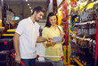 © Studio Romantic - Young married couple in a home goods store standing at a showcase with different tools and looking at list on paper in her hands for choosing various tools for home repairs and other work.