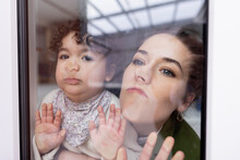 Mother And Daughter Looking Through Window Pressing Faces On Glass Pane