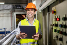 Happy Worker Wearing Hardhat Standing With Tablet PC In Warehouse