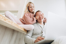 Daughter Covering Eyes Of Father Sitting With Laptop At Home