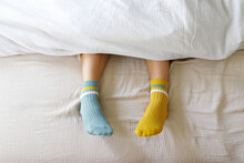 Woman Wearing Blue And Yellow Socks In Bed At Home