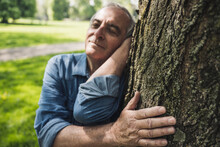 Retired Senior Man With Eyes Closed Leaning On Tree Trunk At Park