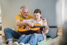 Happy Senior Man Teaching Guitar To Granddaughter At Home