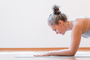 Side view of the senior healthy woman workout at home, making exercise, doing yoga, standing at the plank. Home fitness concept