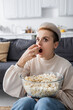 astonished woman watching tv and eating popcorn at home