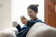 © Natee Meepian - Cheerful young asian woman using mobile phone while sitting on a couch at home.