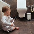 Toddler baby boy is playing in the toilet room with a brush. Child plays on the brown floor in the beige bathroom