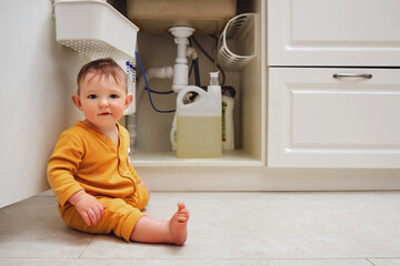 Wall Mural - Toddler baby boy is playing with detergents and cleaning products in an open kitchen cabinet. Child safety issues in the home room, little kid