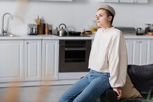 Dreamy Woman In White Pullover Sitting In Kitchen And Looking Away