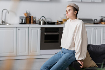 Wall Mural - dreamy woman in white pullover sitting in kitchen and looking away
