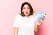 © Asier - Young caucasian woman holding banknotes isolated on pink background shrugs shoulders and open eyes confused.
