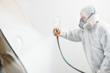 Wall Mural - Male repairman painter in chamber painting automobile car elements. Worker paints the vehicle in white with a spray gun.