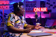 © AnnaStills - Side view of handsome young African American guy wearing headphones sitting at desk recording podcast or broadcast in home studio