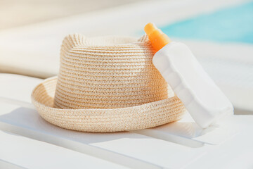 summer straw hat and sunblock on white sun lounger near pool, vacation concept