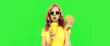 Portrait of young woman drinking fresh juice with fast food, burger wearing yellow t-shirt, sunglasses on green background