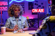 © AnnaStills - Stylish young African American woman sitting at desk in front of male co-worker discussing something during podcast or broadcast recording