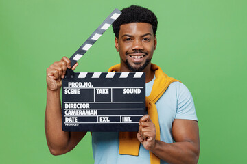 Wall Mural - Young smiling happy man of African American ethnicity 20s wear blue t-shirt holding classic black film making clapperboard isolated on plain green background studio portrait. People lifestyle concept.