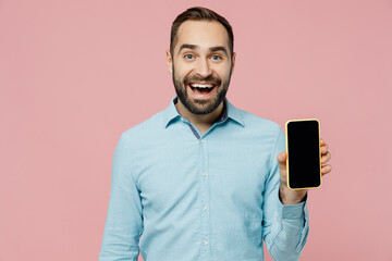 Wall Mural - Young amazed man 20s in classic blue shirt hold in hand use mobile cell phone with blank screen workspace area isolated on plain pastel light pink background studio portrait. People lifestyle concept.