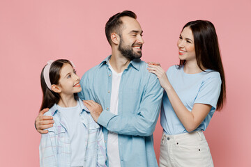 Wall Mural - Young happy smiling cool parents mom dad with child kid daughter teen girl in blue clothes look to each other isolated on plain pastel light pink background Family day parenthood childhood concept.