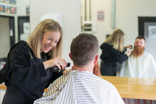 A Happy Woman Barber Trimming Hair Off The Back Of A Man's Neck