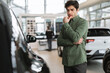 Pensive young guy thinking, making choice, having doubt about buying new car at dealership centre, copy space
