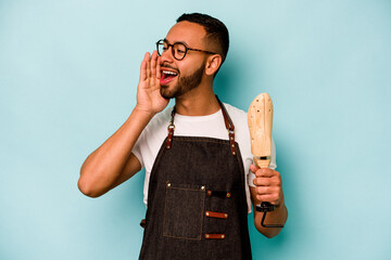 Wall Mural - Young hispanic shoemaker man isolated on blue background shouting and holding palm near opened mouth.