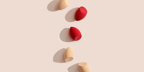 Canvas Print - Wide banner with makeup sponges for foundation cream on beige background with dark shadows. Beauty blender red and beige. Fashion Flat lay cosmetic sponge in row, top view make up puff