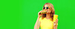 Portrait of happy smiling young woman with fast food, burger and cup of juice wearing yellow t-shirt, sunglasses on green background