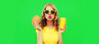 Portrait of young woman with fast food, burger and cup of juice posing wearing yellow t-shirt, sunglasses on green background