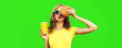 Portrait of young woman with fast food, burger and cup of juice posing wearing yellow t-shirt, sunglasses on green background
