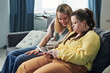 © AnnaStills - Modern young woman with Down syndrome spending time with her sister at home watching content in social net on digital tablet