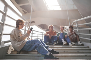 Airy shot of diverse group of teenagers sitting on metal stairs outdoors in urban setting