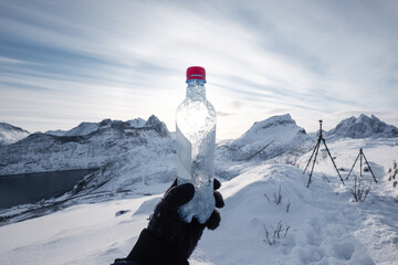 Wall Mural - hand of mountaineer holding water bottle on snow covered mountain in the morning