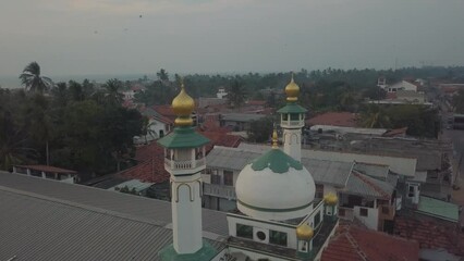 Wall Mural - a white and green Mosque in Sri Lanka with grand towers and dome with golden details in a city surrounded by residential buildings on a sunny afternoon